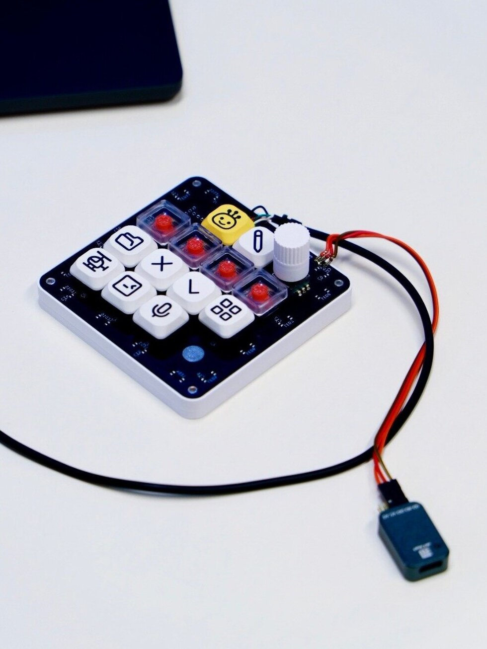The first hand-built OpenMicroKbd prototype: black PCB, white 3D-printed case, red low-profile switches and a placeholder knob, cabled to a debug adapter